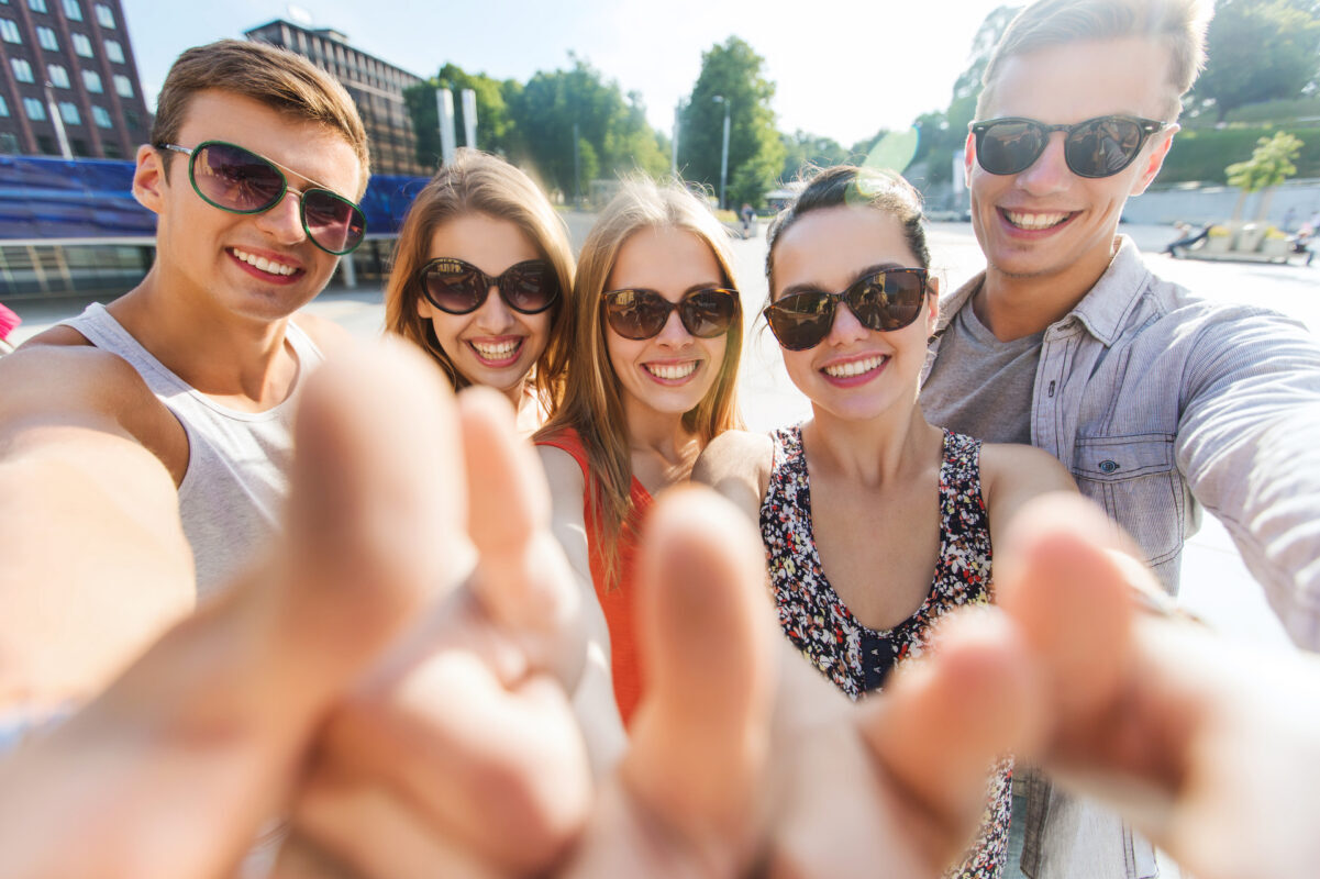 tourism, travel, people, leisure and technology concept - group of smiling teenage friends taking selfie and showing thumbs up outdoors