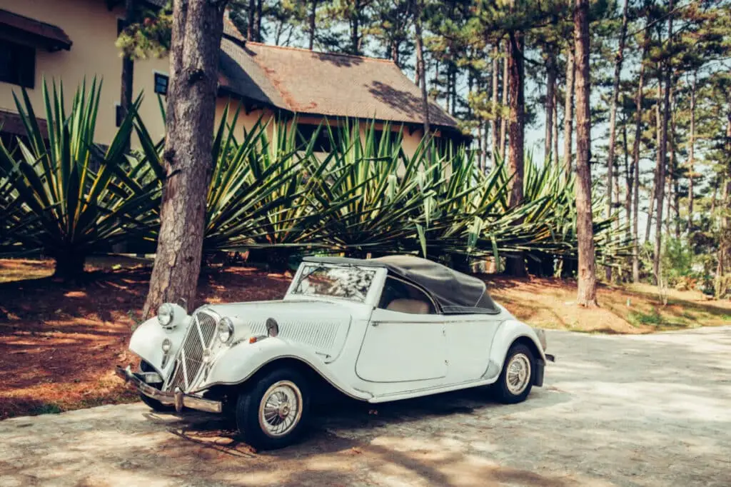 Spain - Warm atmosphere and light through pine tree with white vintage luxury classic convertible car at colonial villa