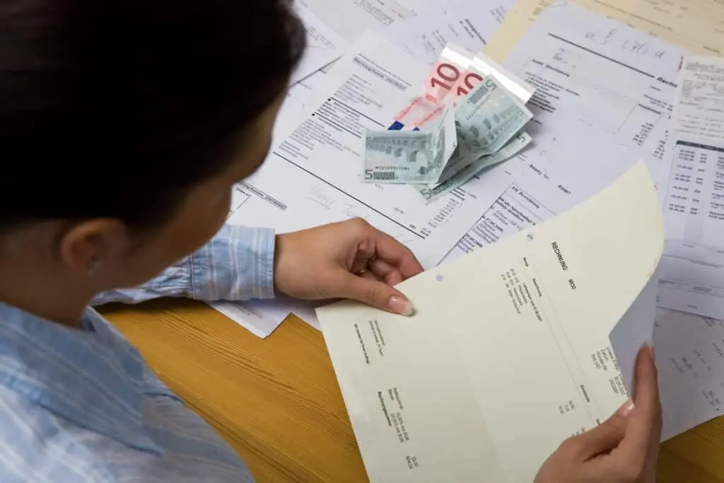 A person reviewing bills and cash on a wooden table, with various documents and euro banknotes visible