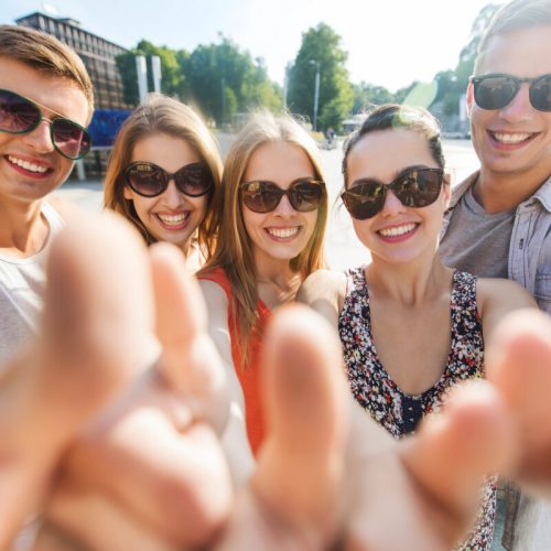 tourism, travel, people, leisure and technology concept - group of smiling teenage friends taking selfie and showing thumbs up outdoors