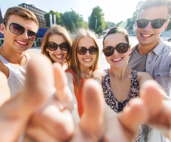 tourism, travel, people, leisure and technology concept - group of smiling teenage friends taking selfie and showing thumbs up outdoors