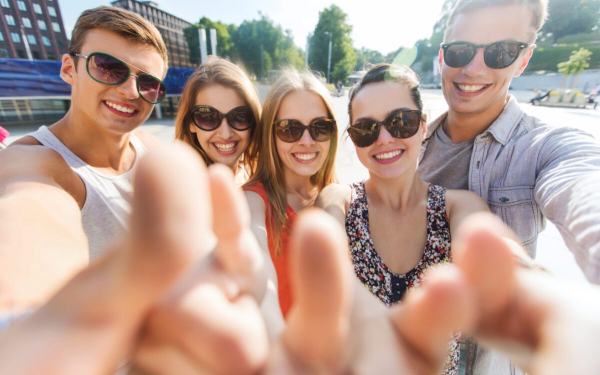 tourism, travel, people, leisure and technology concept - group of smiling teenage friends taking selfie and showing thumbs up outdoors